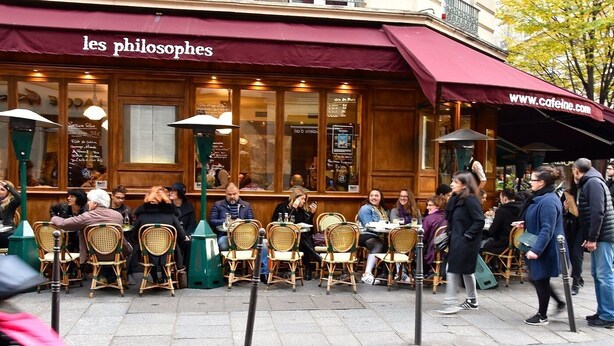 An outdoor café with wicker chairs and tables, a maroon awning, and a visible website address. - A CENTRAL PARISIAN EXPERIENCE WITH MODERN CONVENIENCES IN THE ICONIC LE MARAIS (Paris)