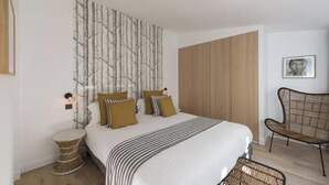 A modern bedroom with a large bed, a wall-mounted tree design, a wooden wardrobe, and a wicker chair. - A CENTRAL PARISIAN EXPERIENCE WITH MODERN CONVENIENCES IN THE ICONIC LE MARAIS (Paris)