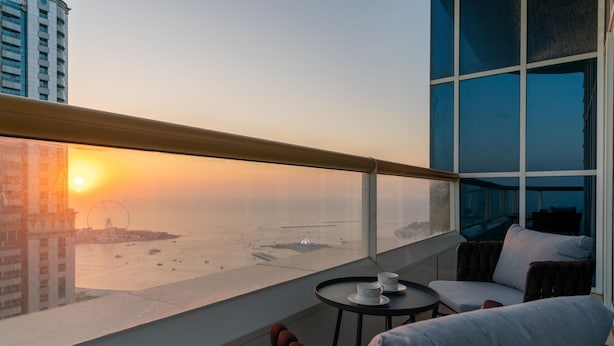 A balcony with a view of the sunset over the water, a table with two cups, and a sofa with cushions. - 4BR Maid Penthouse w Pool and Jacuzzi (Dubai)