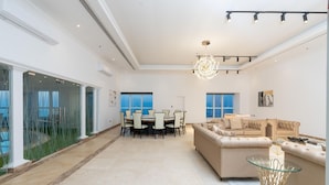 A spacious living area with a large sofa, a glass coffee table, and a dining table with chairs. There are large windows providing a view of the outdoors. - 4BR Maid Penthouse w Pool and Jacuzzi (Dubai)