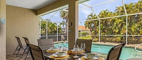 Un área de comedor al aire libre con vista a la piscina, que incluye una mesa con platos, vasos y sillas.
