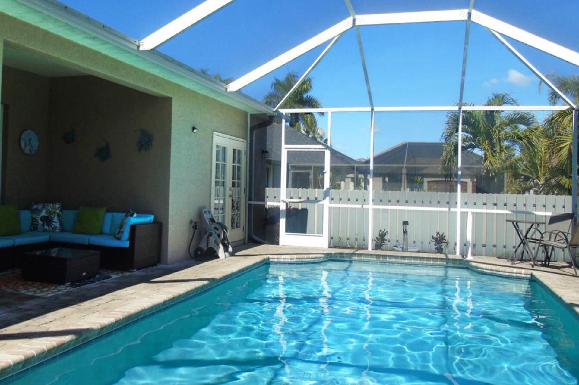 A swimming pool with a covered patio area, a white fence, and a green building.