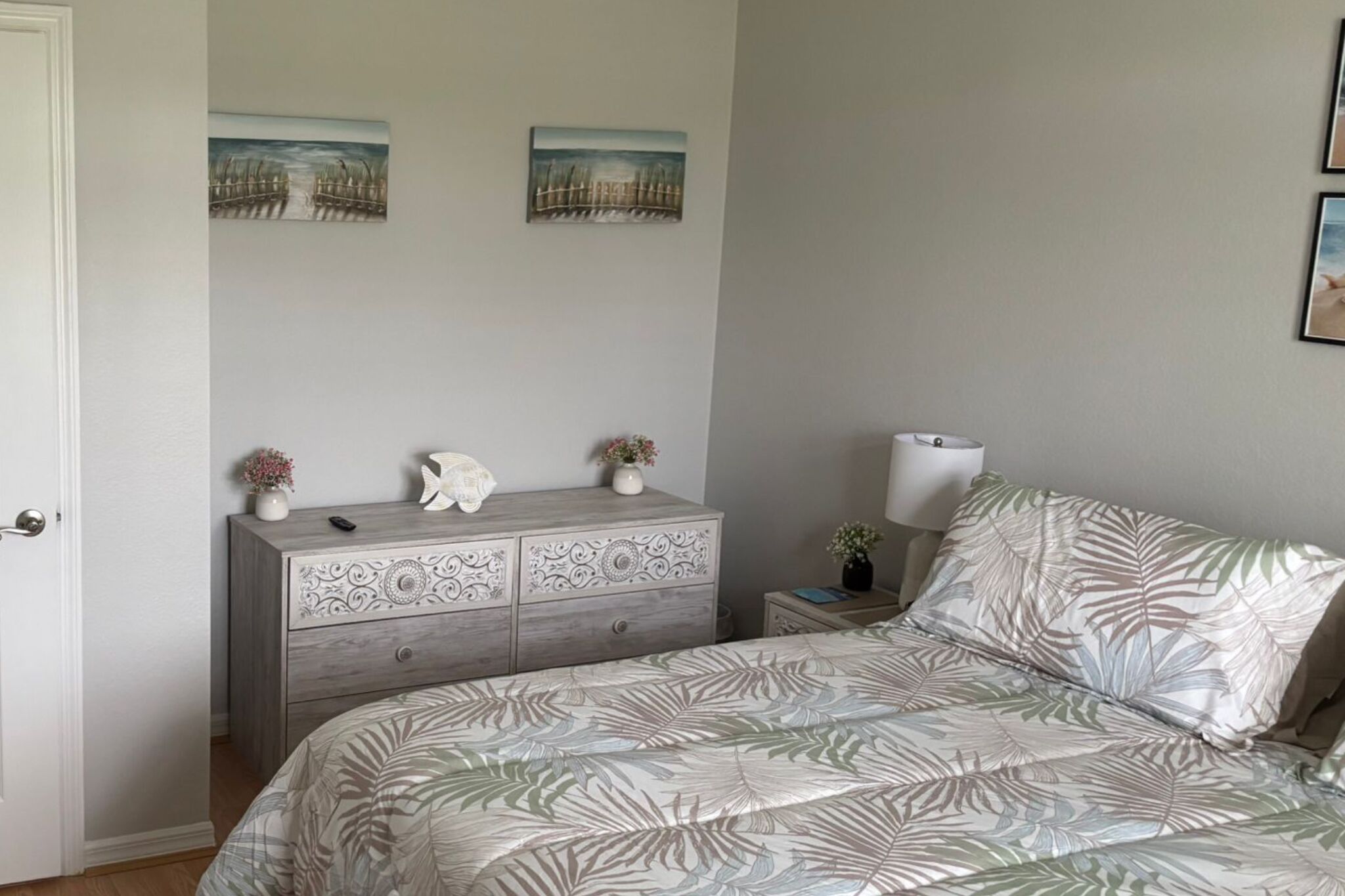 Une chambre à coucher comprenant un lit, une commode, deux tableaux accrochés au mur et une table de chevet avec une lampe.