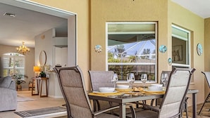 Uma área de refeições ao ar livre com uma mesa posta para quatro pessoas, rodeada por cadeiras.