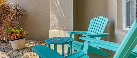 Uma cadeira Adirondack turquesa e uma mesa combinando num alpendre, com uma planta em vaso e uma parede texturizada.