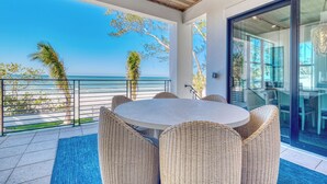 Ein Balkon mit Korbmöbeln, einer Glastür und Blick aufs Meer.