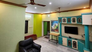 A living room with a sofa, TV stand, and ceiling fan. - Holiday Home - GF 3BHK Full House (Madurai)