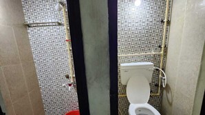 A small bathroom with a toilet, a shower, and a red bucket on the floor. - Holiday Home - GF 3BHK Full House (Madurai)