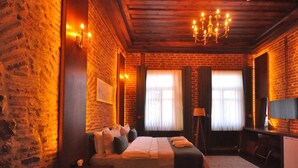 A cozy room with a brick wall, a bed with pillows, a chandelier, and a TV on a stand. - Mihman Konak Hotel (Kars)