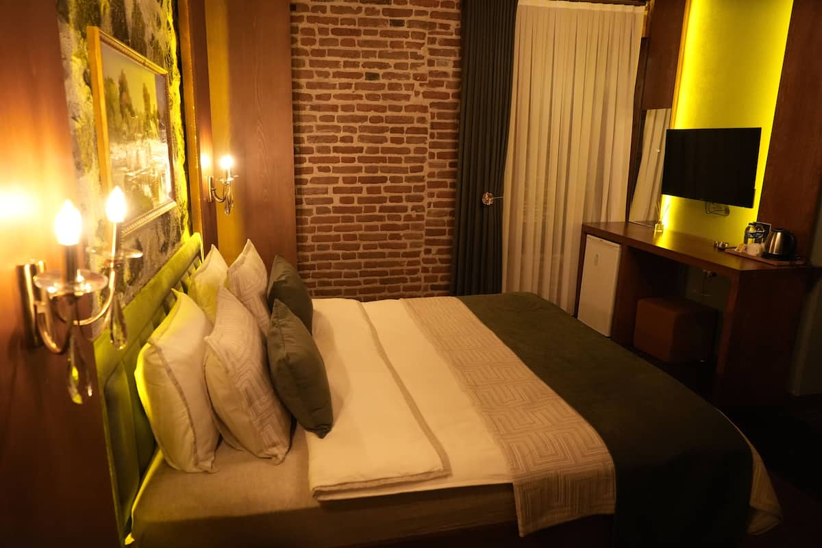 Quarto de hotel com parede de tijolos, cama com travesseiros, escrivaninha com abajur e televisão.