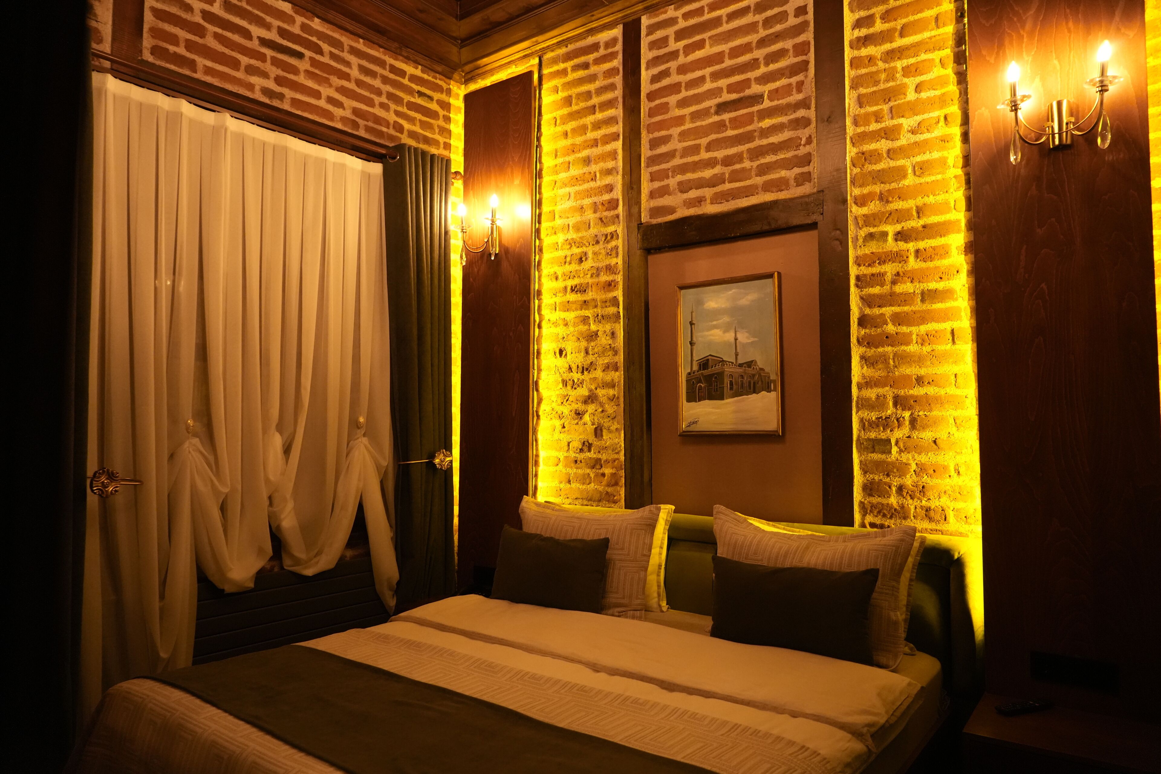 A hotel room with a brick wall, a bed with a white comforter, and a painting on the wall.