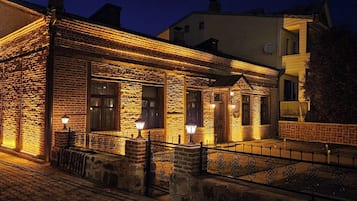 Un edificio de piedra con fachada de ladrillo, iluminado con luz cálida, que presenta una barandilla metálica y un acceso empedrado.