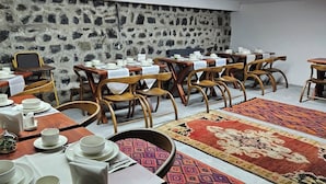 A dining area with multiple tables set for service, stone walls, and patterned rugs. - Mihman Konak Hotel (Kars)