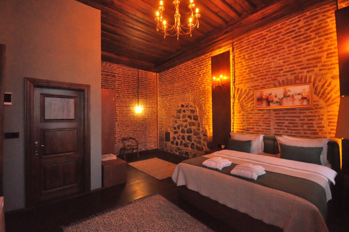 A hotel room with a brick wall, a chandelier, a bed with pillows, and a door.