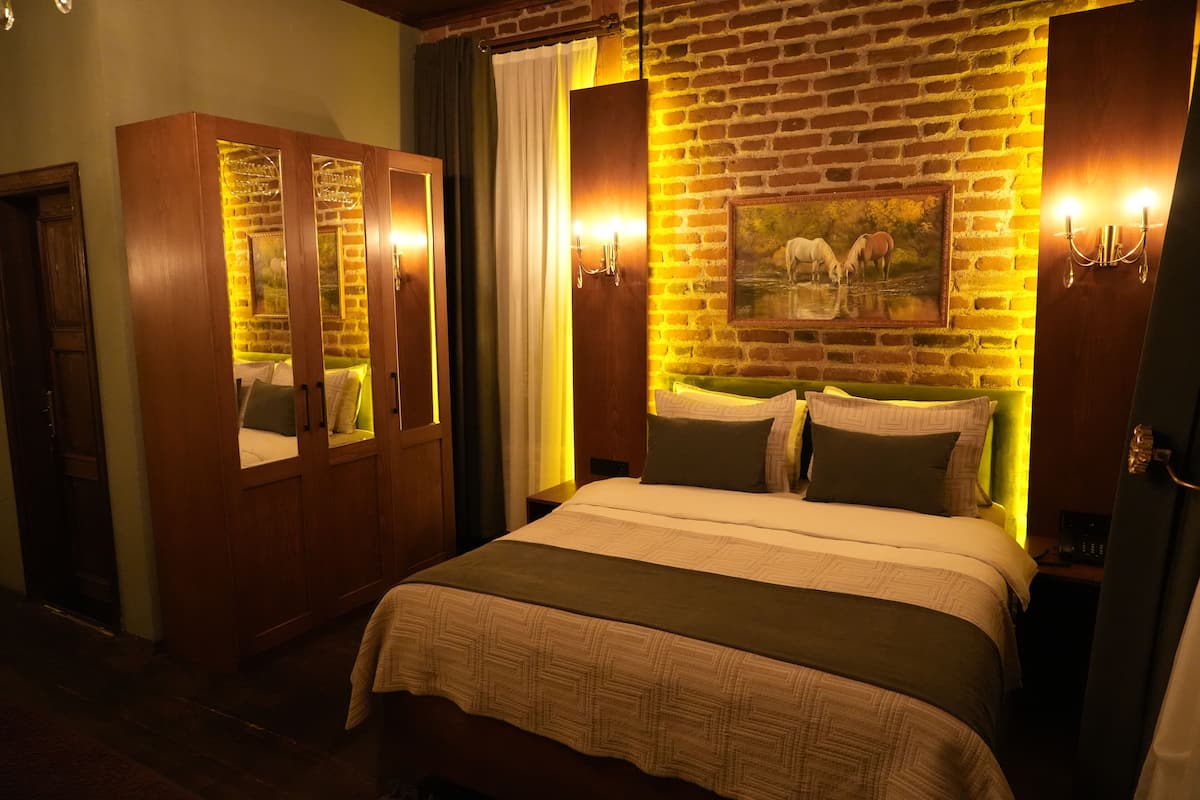Quarto de hotel com parede de tijolos, cama com colcha estampada, guarda-roupa de madeira e um quadro com cavalos.