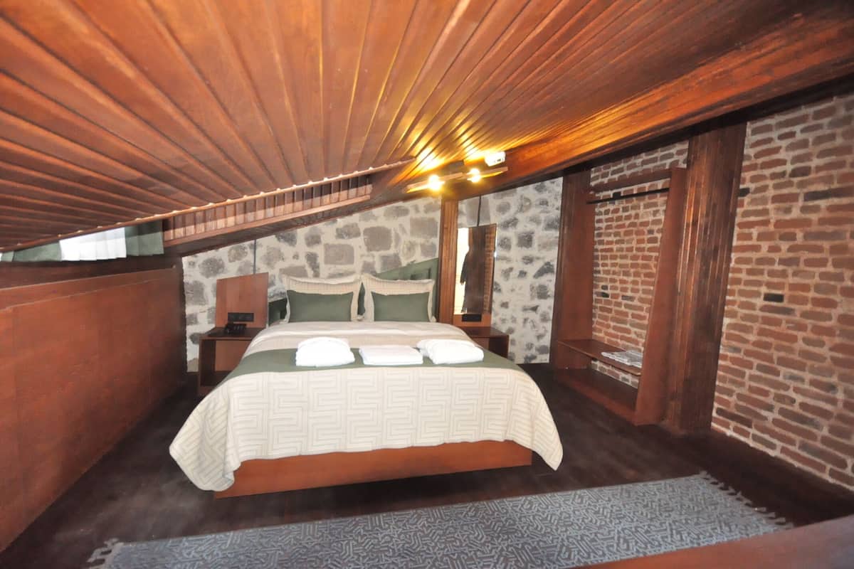 Quarto com teto de madeira, parede de tijolos e cama com colcha estampada.