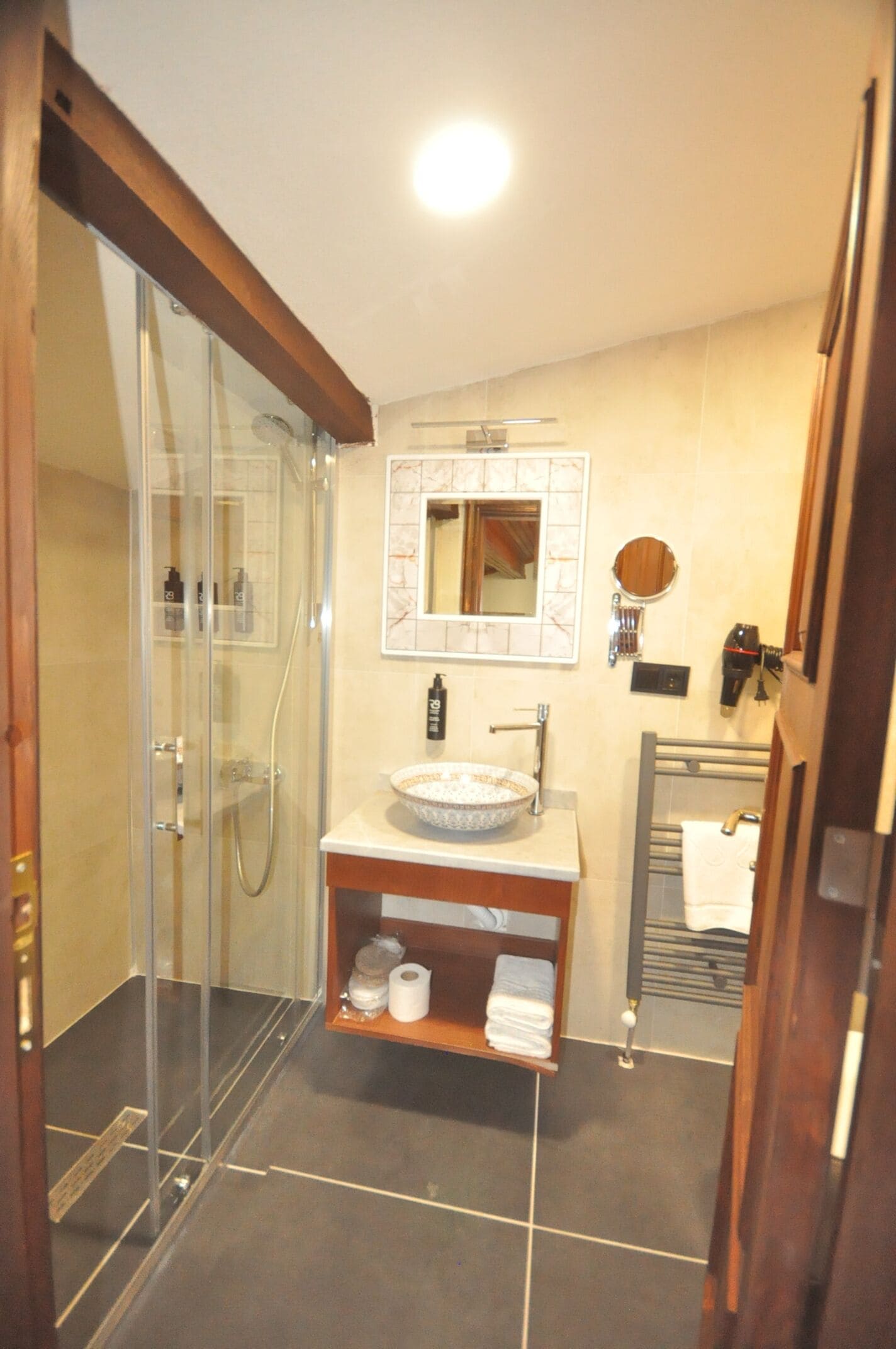 A bathroom with a glass shower enclosure, a sink with a marble countertop, a mirror above the sink, and a towel rack.