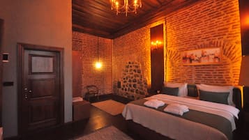 A hotel room with a brick wall, a chandelier, a bed with pillows, and a door.