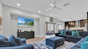A modern living room with a large sectional sofa, a coffee table, and a painting of a beach scene. - Unique, 7 bed Luxury Disney Escape, Theater & Heated Pool (Davenport)