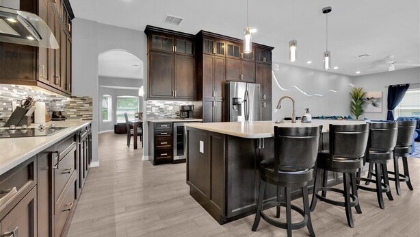 A modern kitchen with dark wood cabinets, stainless steel appliances, and a central island with bar stools. - Unique, 7 bed Luxury Disney Escape, Theater & Heated Pool (Davenport)