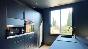 Une cuisine moderne avec des meubles de couleur sombre, un four encastré et une grande fenêtre offrant une vue sur l’extérieur.