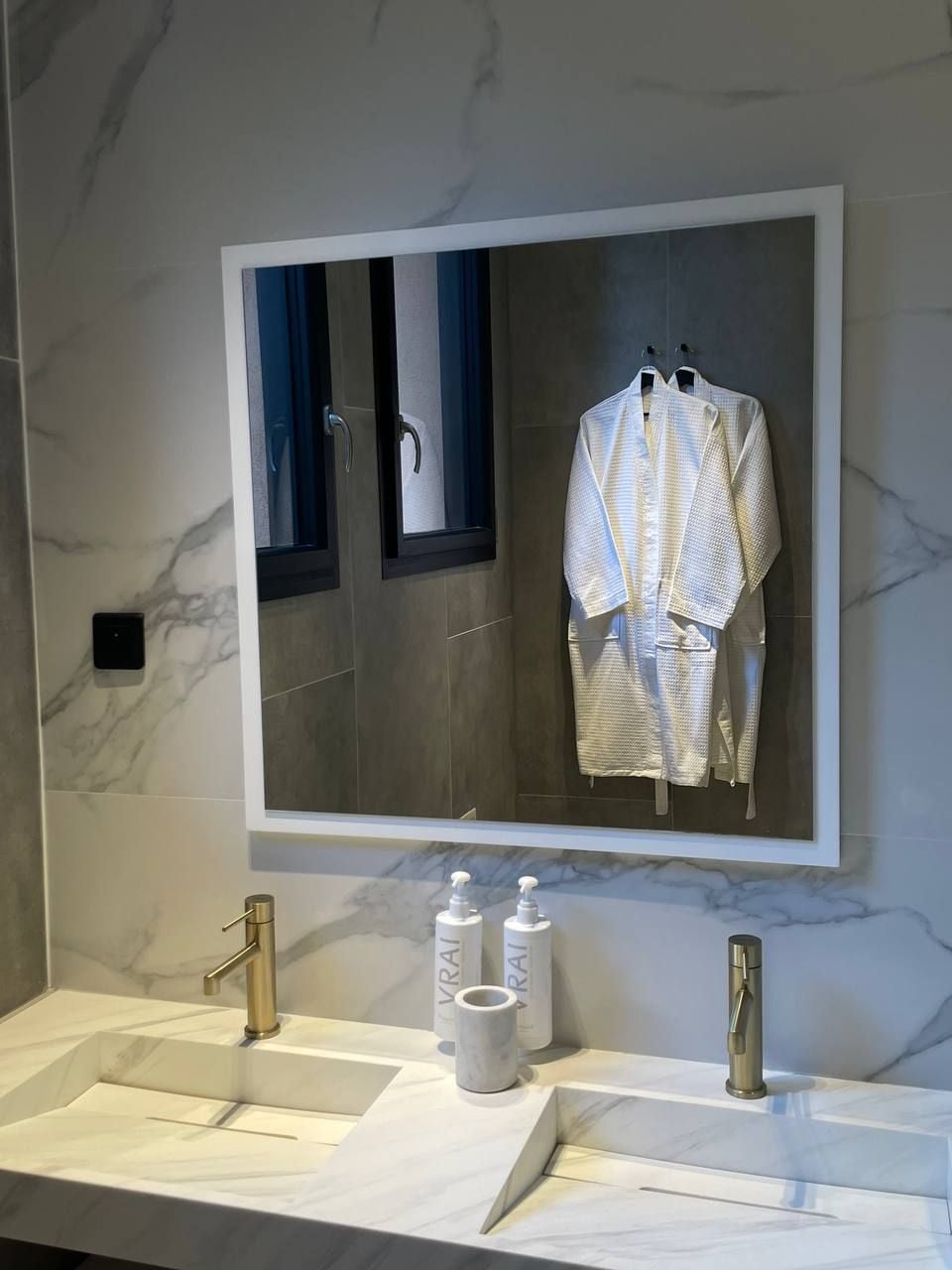Casa de banho com um espelho grande, duas pias e um porta-toalhas com toalhas.