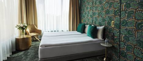 A hotel room with a large bed, a chair, a small table, and a decorative vase.