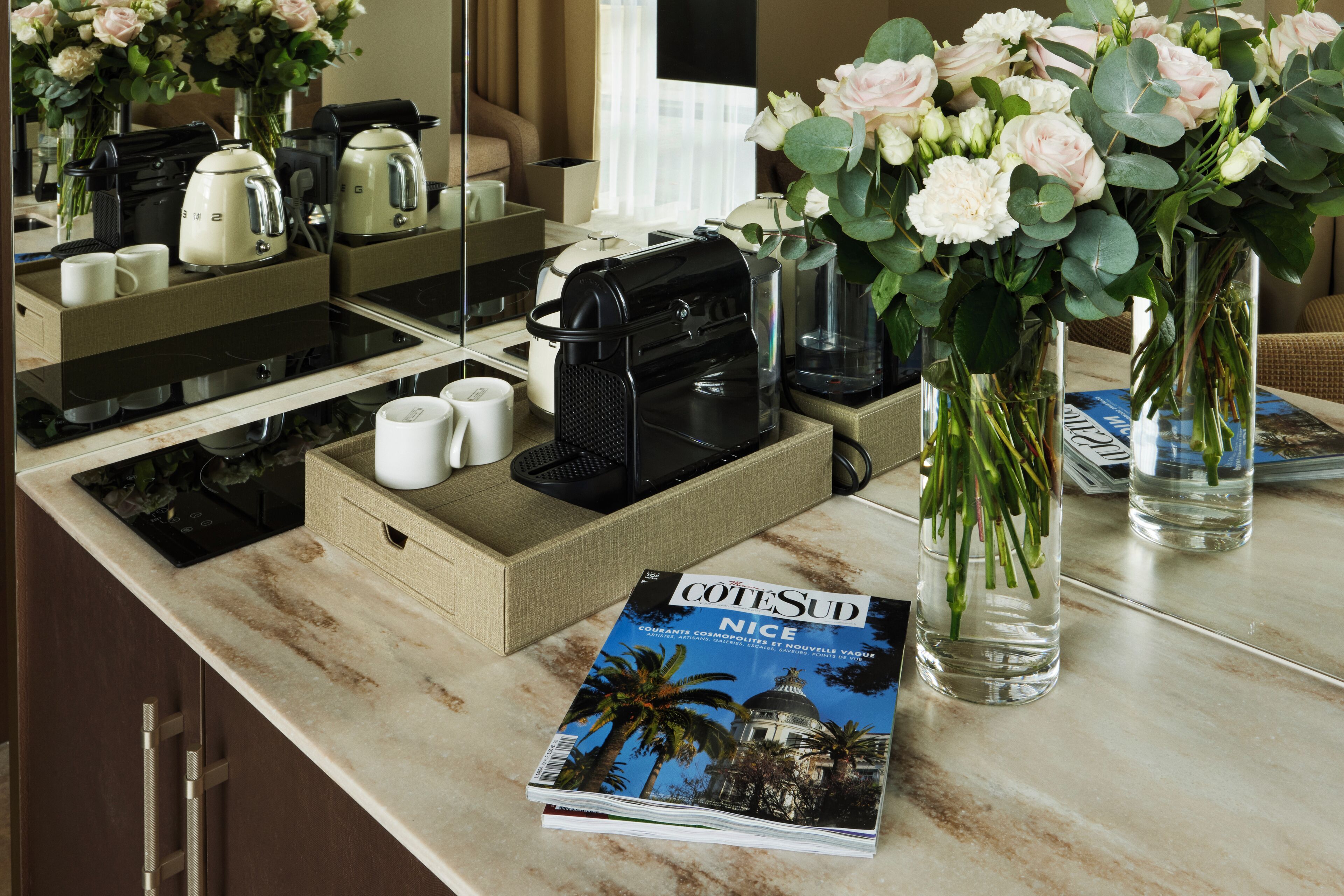 Un comptoir de cuisine d’hôtel avec une machine à café, une bouilloire et un magazine intitulé « COTESUD NICE ».