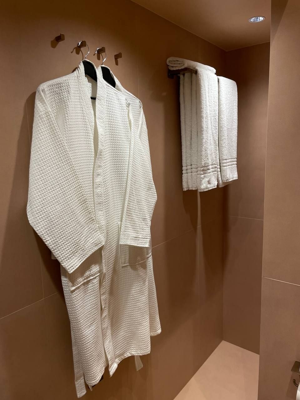 Une salle de bain avec un grand miroir, un porte-serviettes avec deux serviettes et un espace douche.