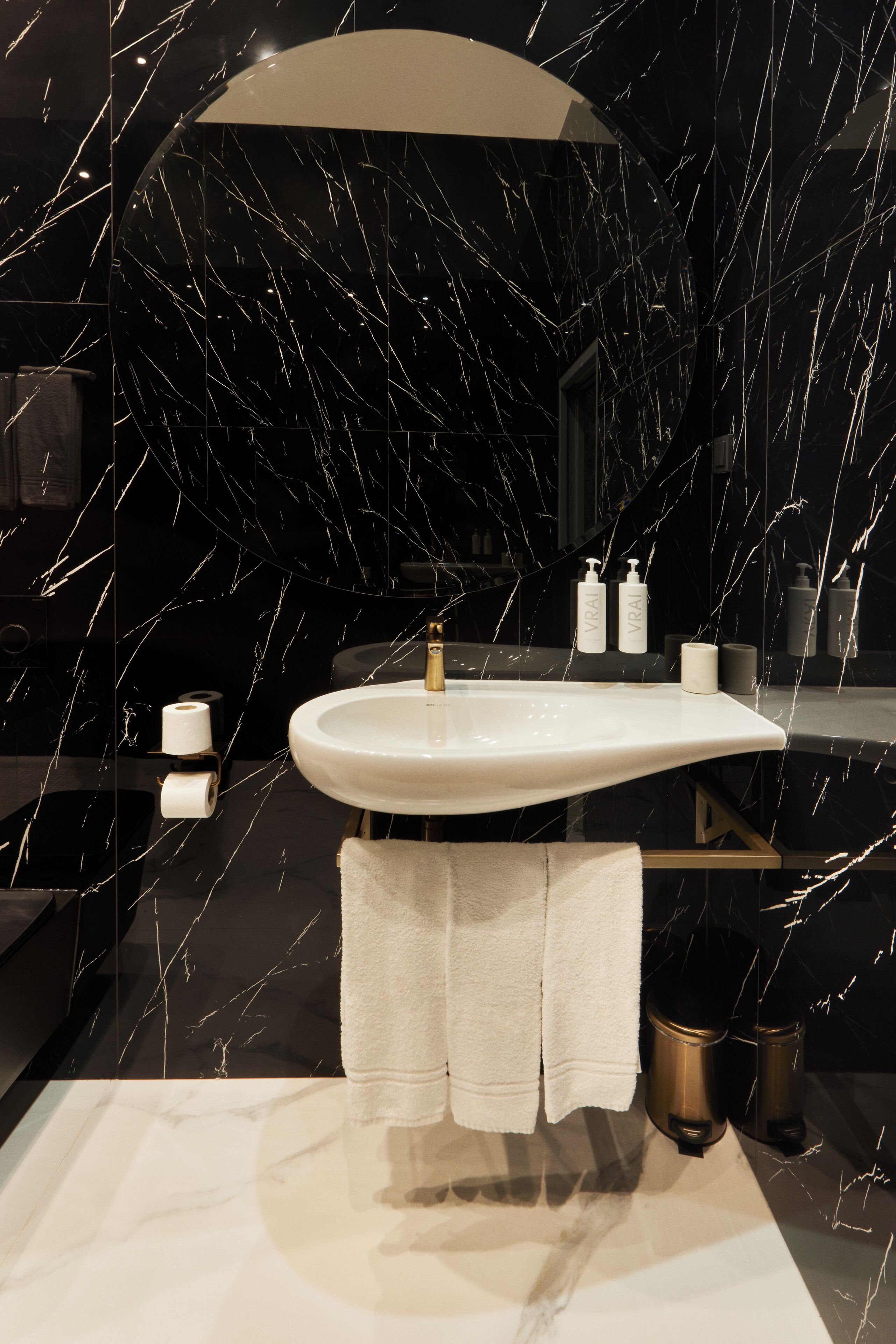 A modern bathroom with a marble sink, two trash bins, and a towel rack.