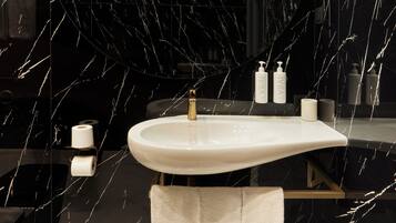 A modern bathroom with a marble sink, two trash bins, and a towel rack.