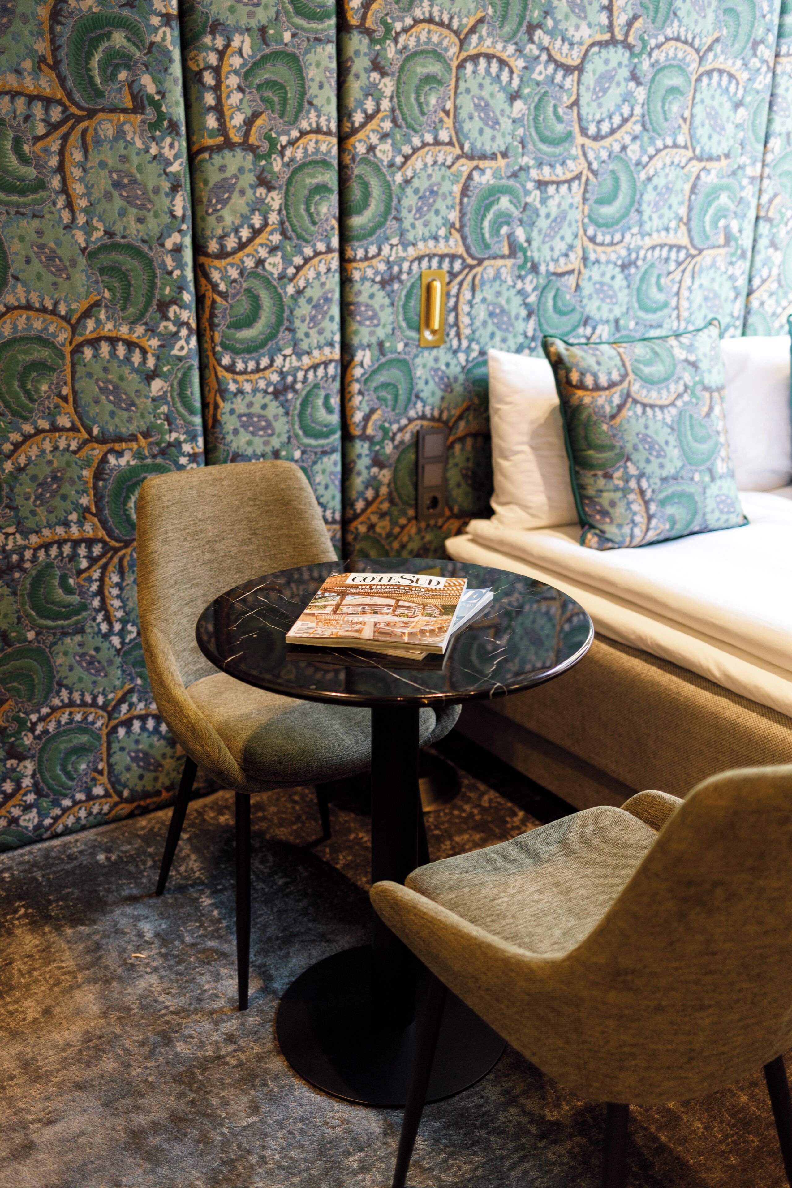 Una habitación con papel tapiz estampado, un sofá, una mesa redonda con una revista y dos sillas.