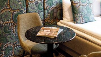 Una habitación con papel tapiz estampado, un sofá, una mesa redonda con una revista y dos sillas.