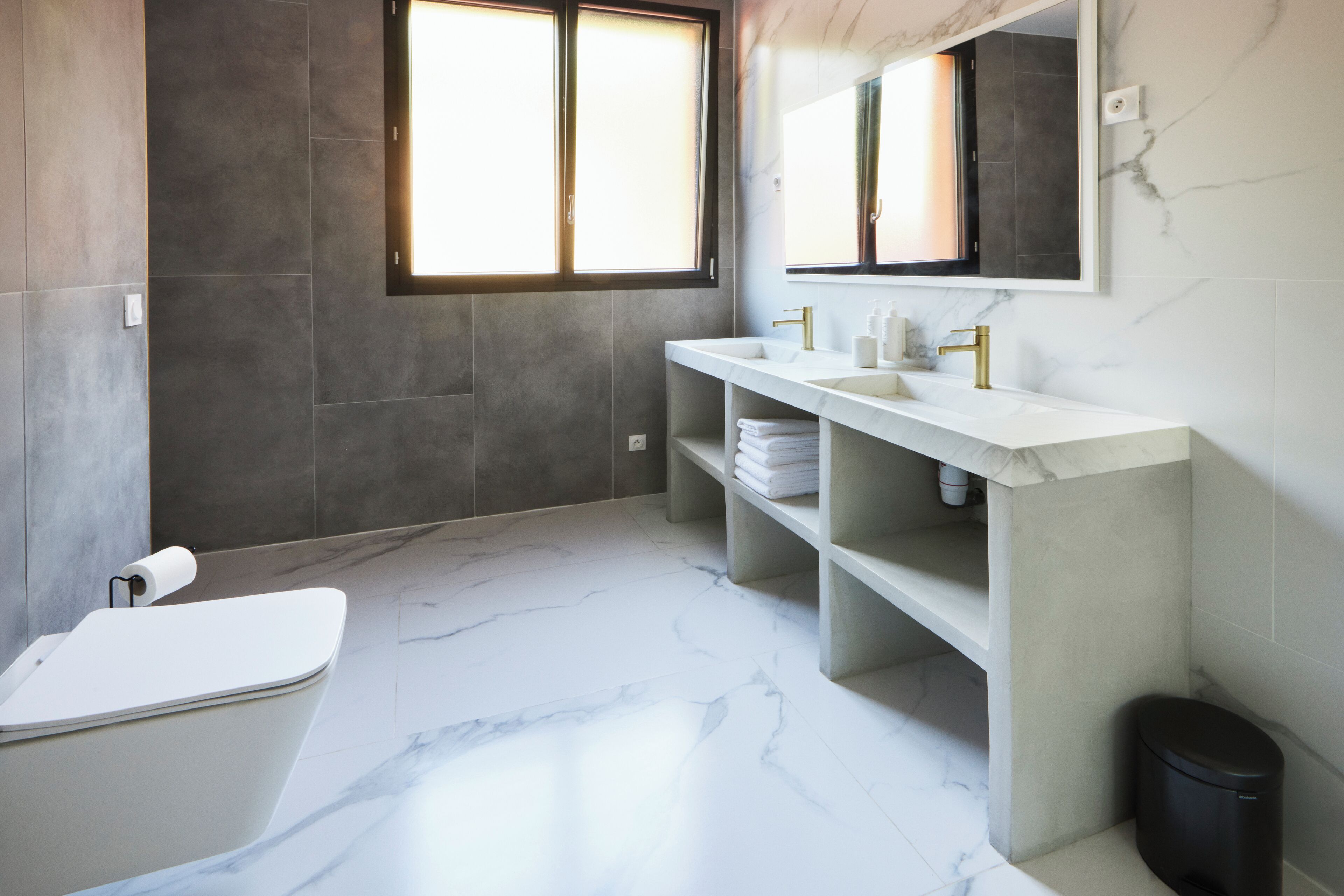 A modern bathroom with a bathtub, two sinks, a large mirror, and a window.