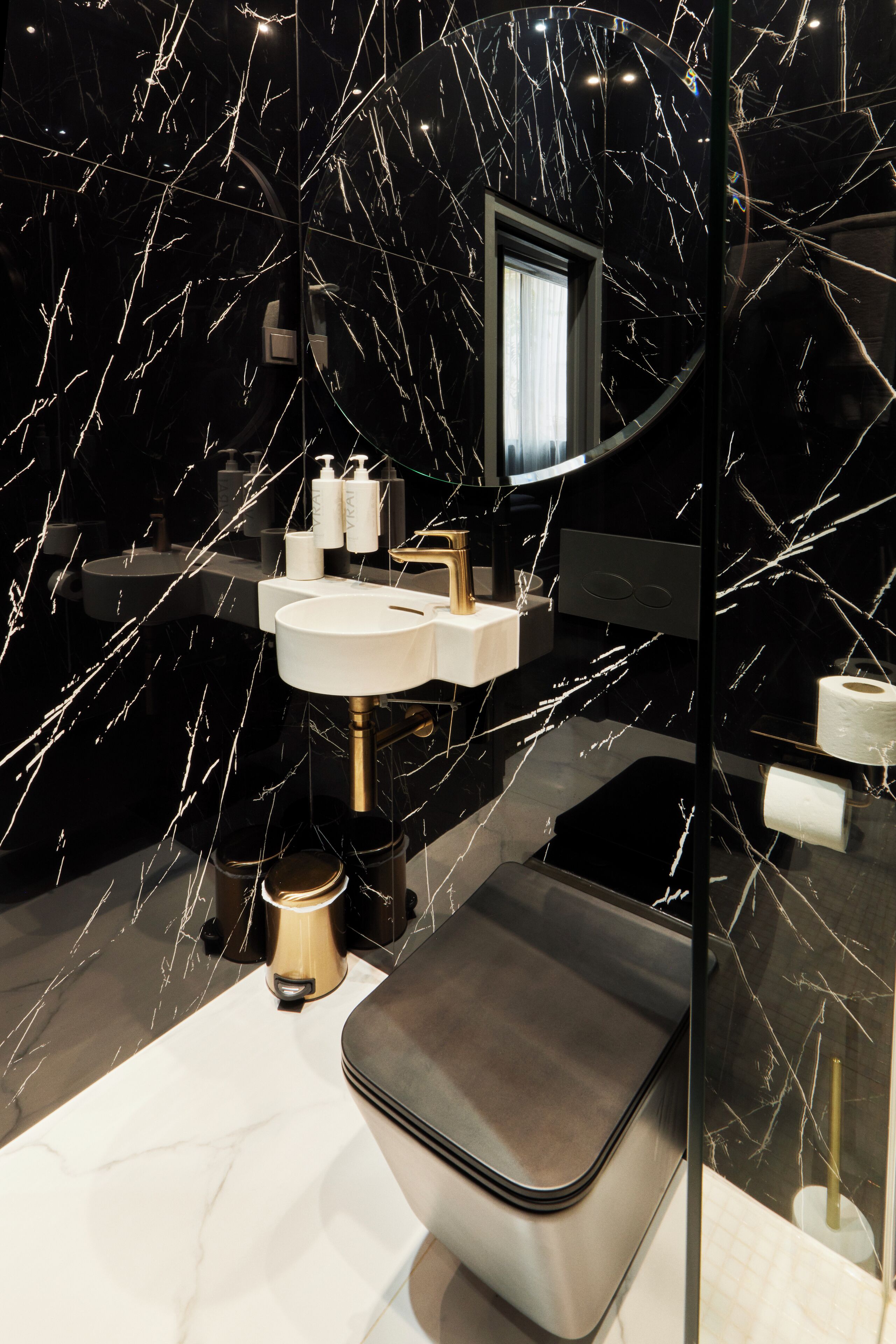 Un baño moderno con salpicadero de mármol negro, un lavabo blanco y un grifo dorado.