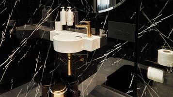 Un baño moderno con salpicadero de mármol negro, un lavabo blanco y un grifo dorado.