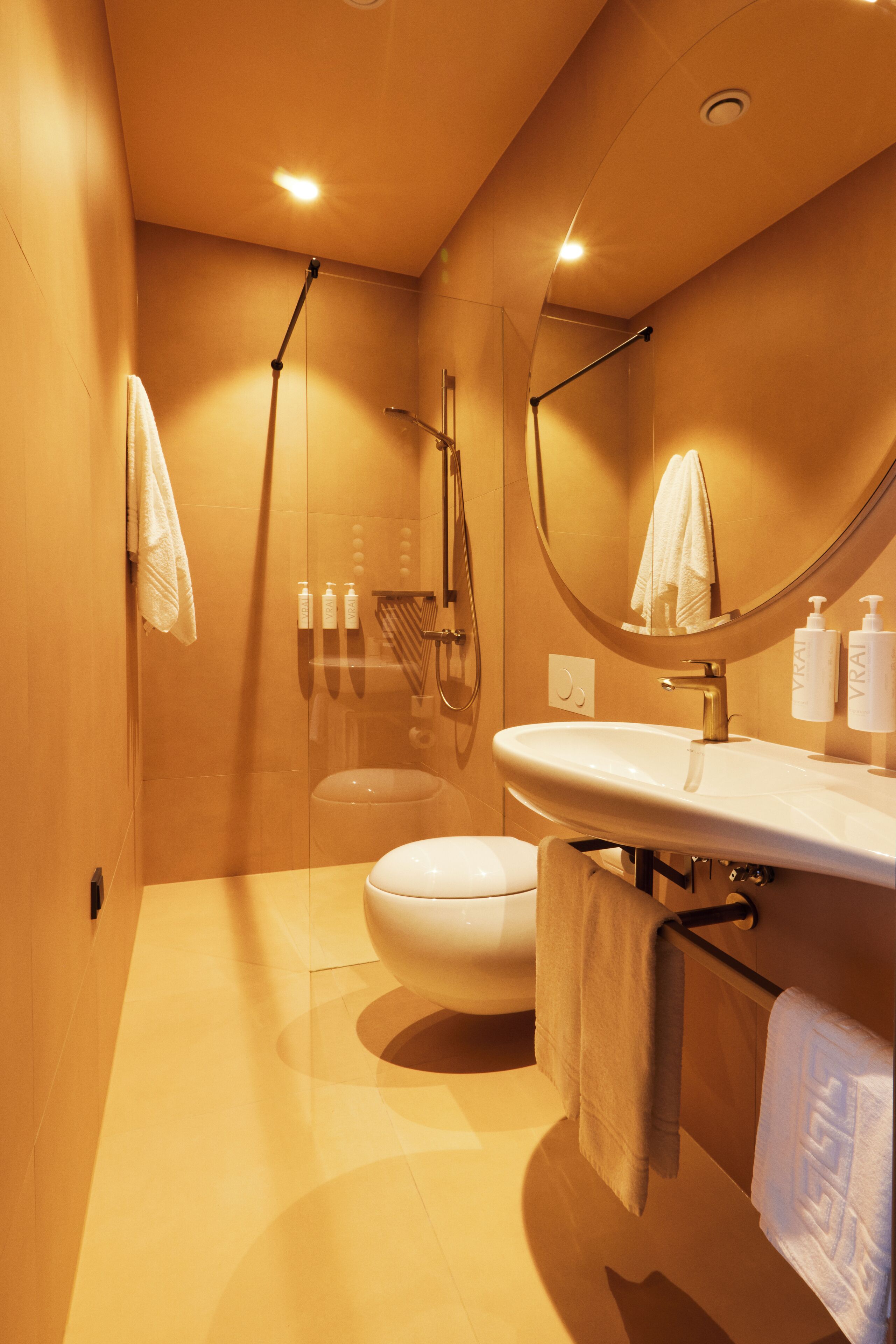 Un baño moderno con inodoro, lavabo, ducha y un espejo grande.