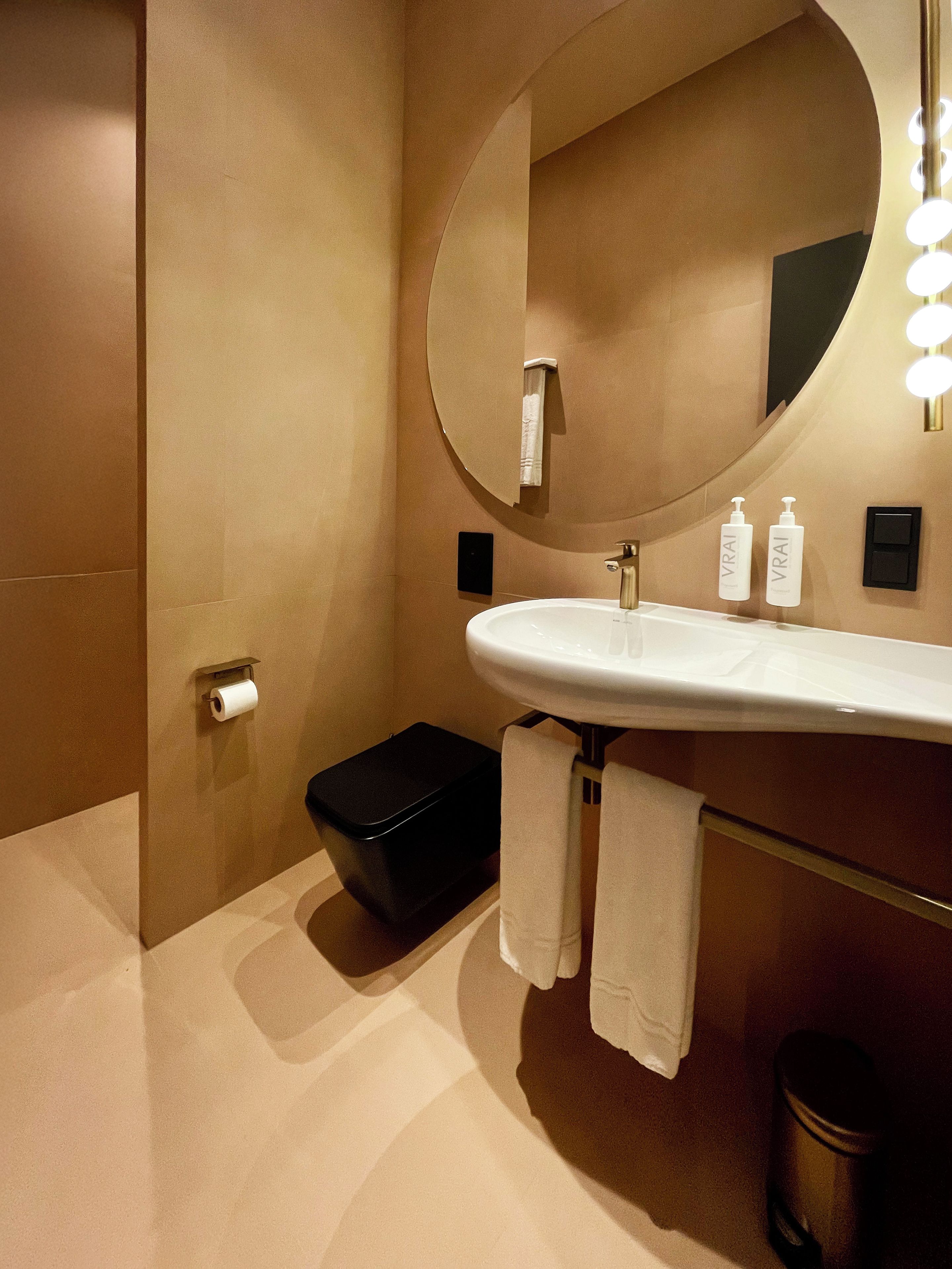 Un baño moderno con un espejo ovalado grande, un lavabo blanco y dos botellas de loción.