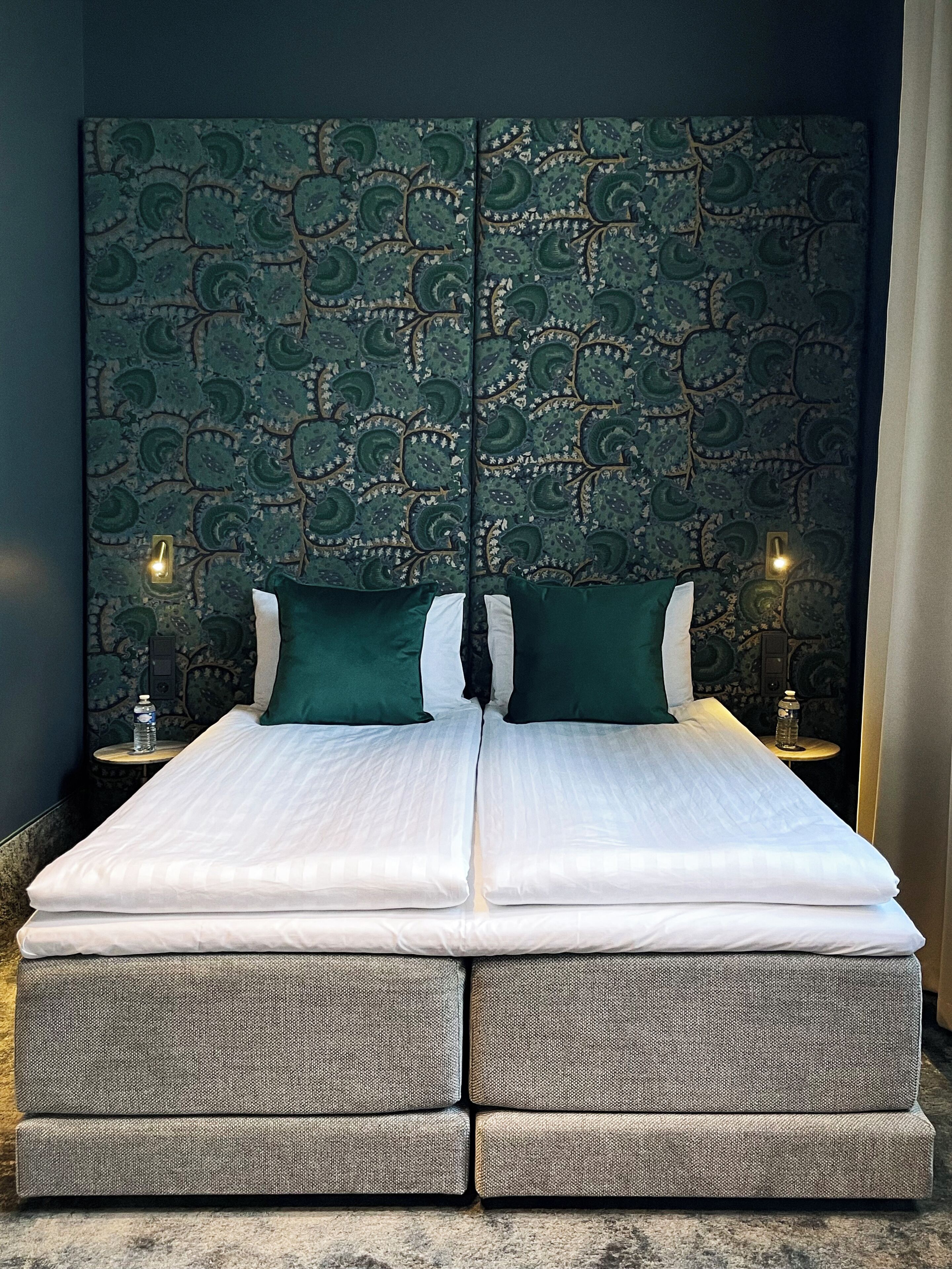 A double bed with a patterned headboard, two bedside tables with lamps, and a water bottle on one table.