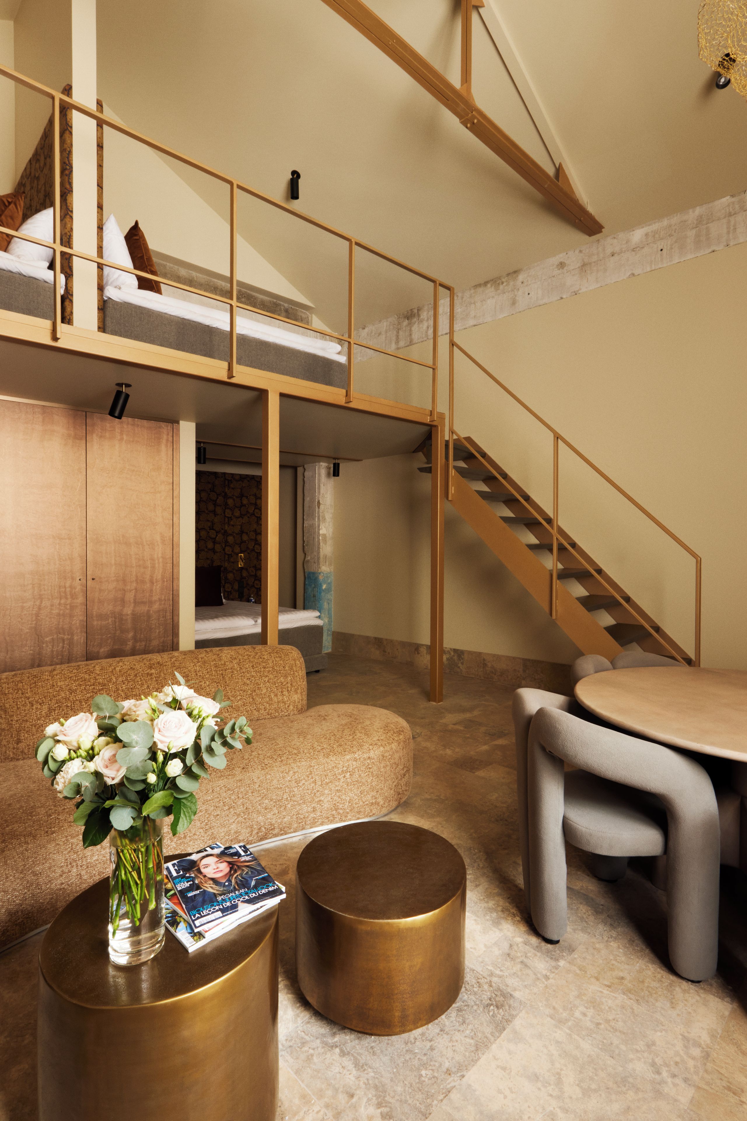 Ein modernes Interieur mit Schlafzimmer im Zwischengeschoss, einer Treppe und einer Sitzecke inklusive Couchtisch und Blumenvase.