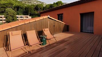Terraza de madera con dos sillones de descanso y una pequeña mesa, con vista a un paisaje montañoso.