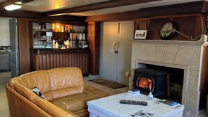Un salon avec un canapé en cuir, une table basse blanche, une cheminée et un coin bar doté d’étagères remplies de bouteilles et de verres.