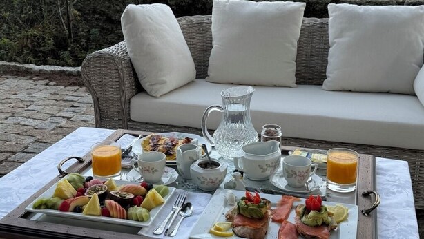Une table dressée pour le petit-déjeuner, placée à l’extérieur, avec un canapé en osier en arrière-plan.