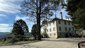 Un grand bâtiment blanc à la façade en pierre, doté d’un escalier central et d’une cour pavée.