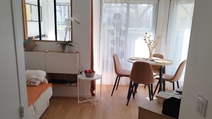 Un espai habitable compacte amb un llit, un escriptori petit, una taula de dinar i una finestra gran.