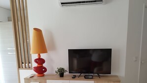 Un saló modern amb televisió sobre un moble de fusta, una planta petita i una làmpada.