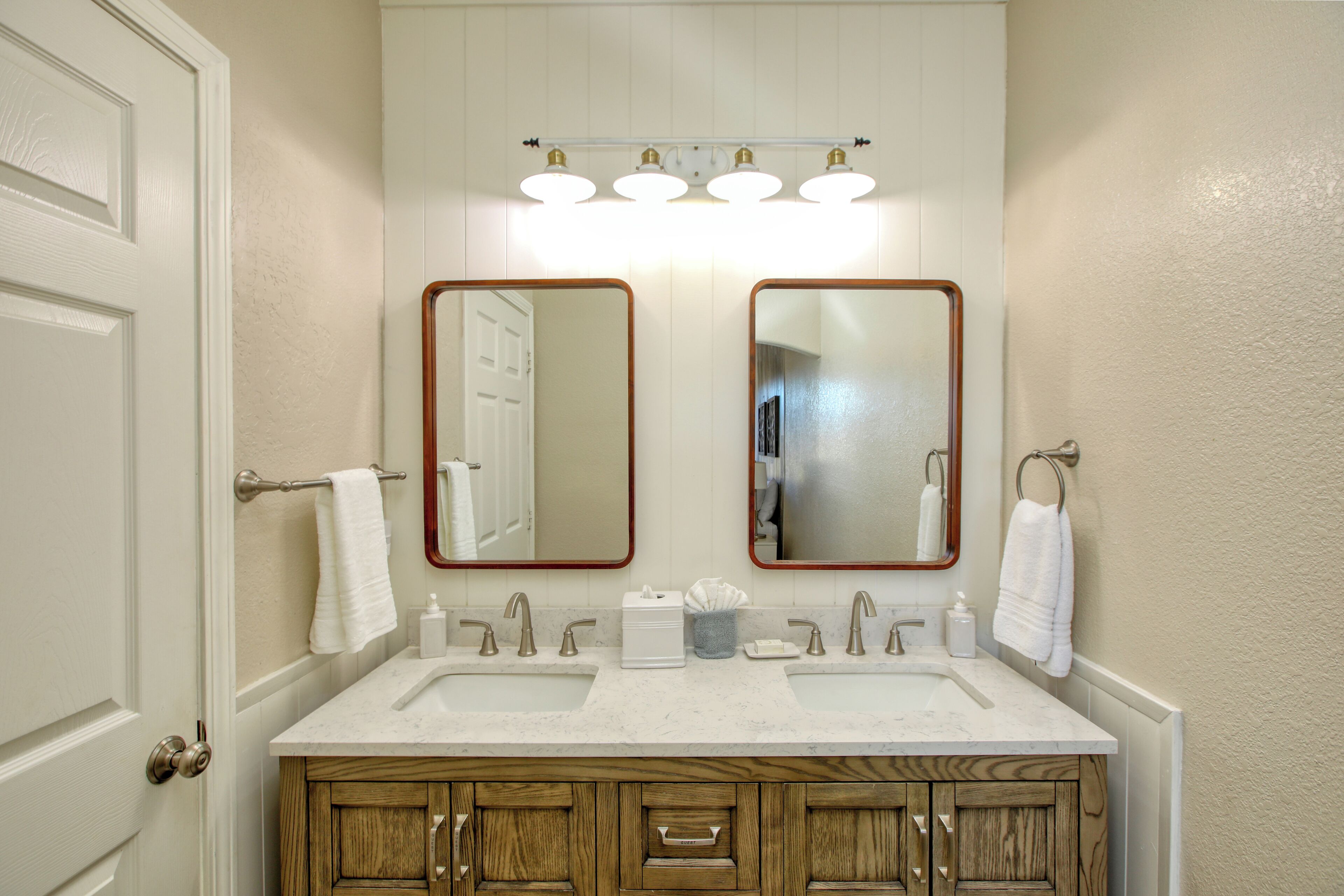 A bathroom with two sinks, wooden cabinets, a towel rack, and a mirror with a light above it.