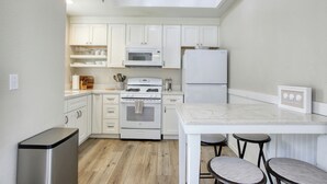 Cocina moderna con armarios blancos, un bote de basura de acero inoxidable, encimera de mármol y una pequeña barra con taburetes.