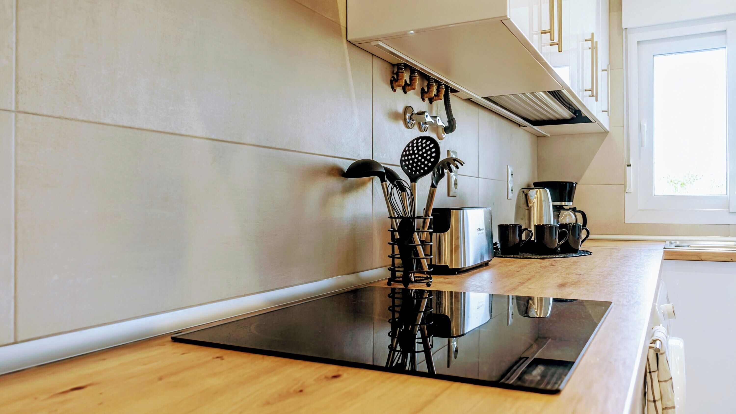 Una cocina moderna con una placa de inducción negra, electrodomésticos de acero inoxidable y una cafetera.
