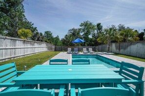 Un patio trasero con piscina, cercado de madera y una mesa con sillas.